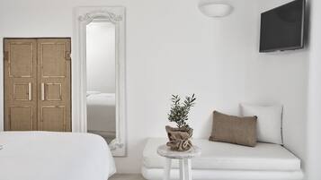 Quarto minimalista com uma cama, uma mesinha redonda com uma planta, um sofá com almofadas, um espelho grande e uma TV de tela plana.