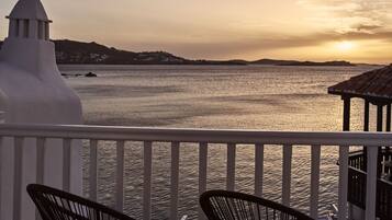 A balcony with two black chairs, a white railing, and a view of the sea at sunset.