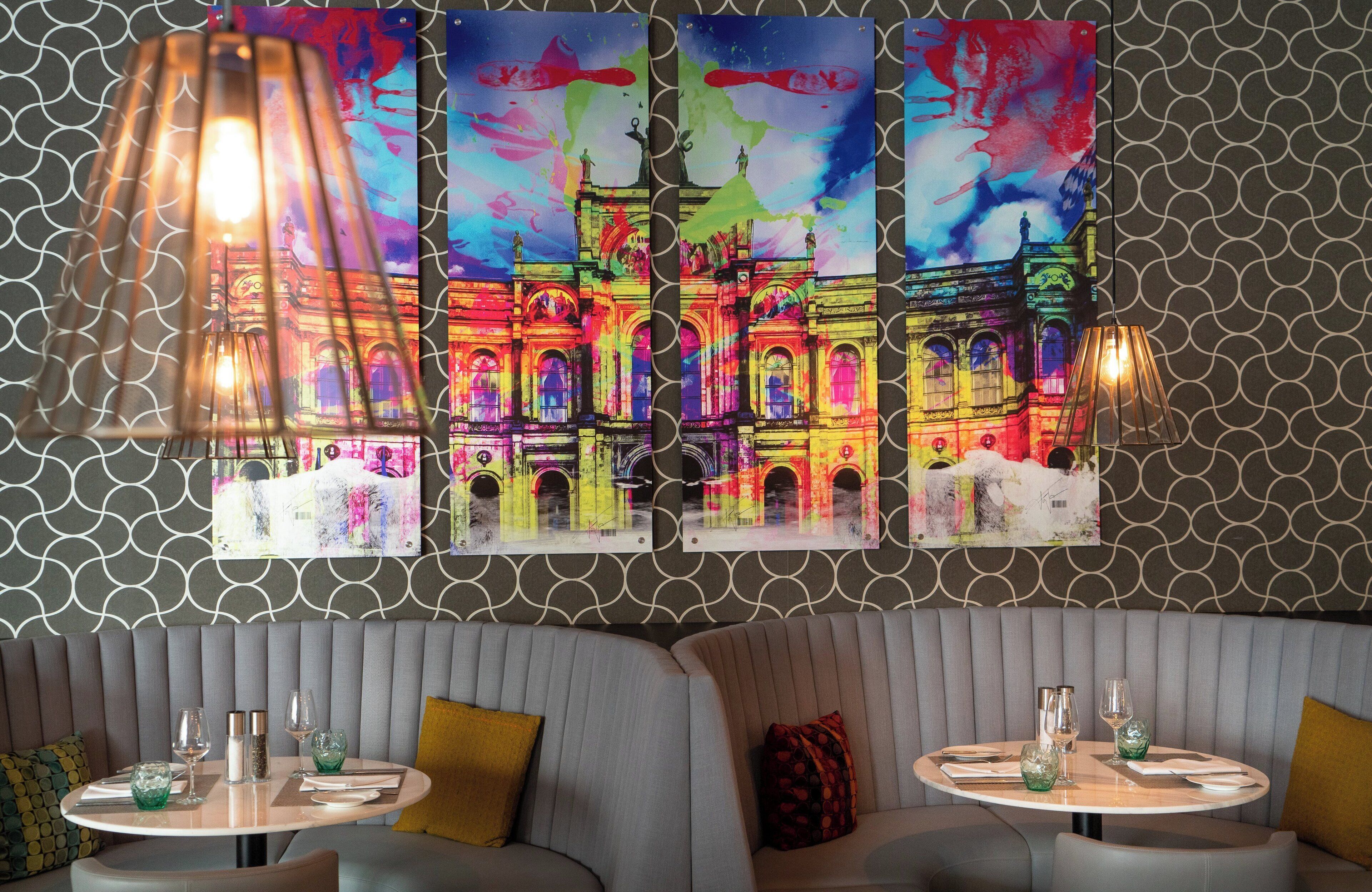 Un restaurante con una decoración moderna, que presenta una pared con diseño, una zona de estar con bancos acolchados y una mesa servida con copas y servilletas.