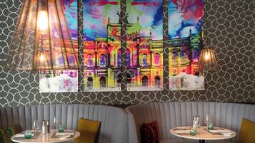 Un restaurante con una decoración moderna, que presenta una pared con diseño, una zona de estar con bancos acolchados y una mesa servida con copas y servilletas.