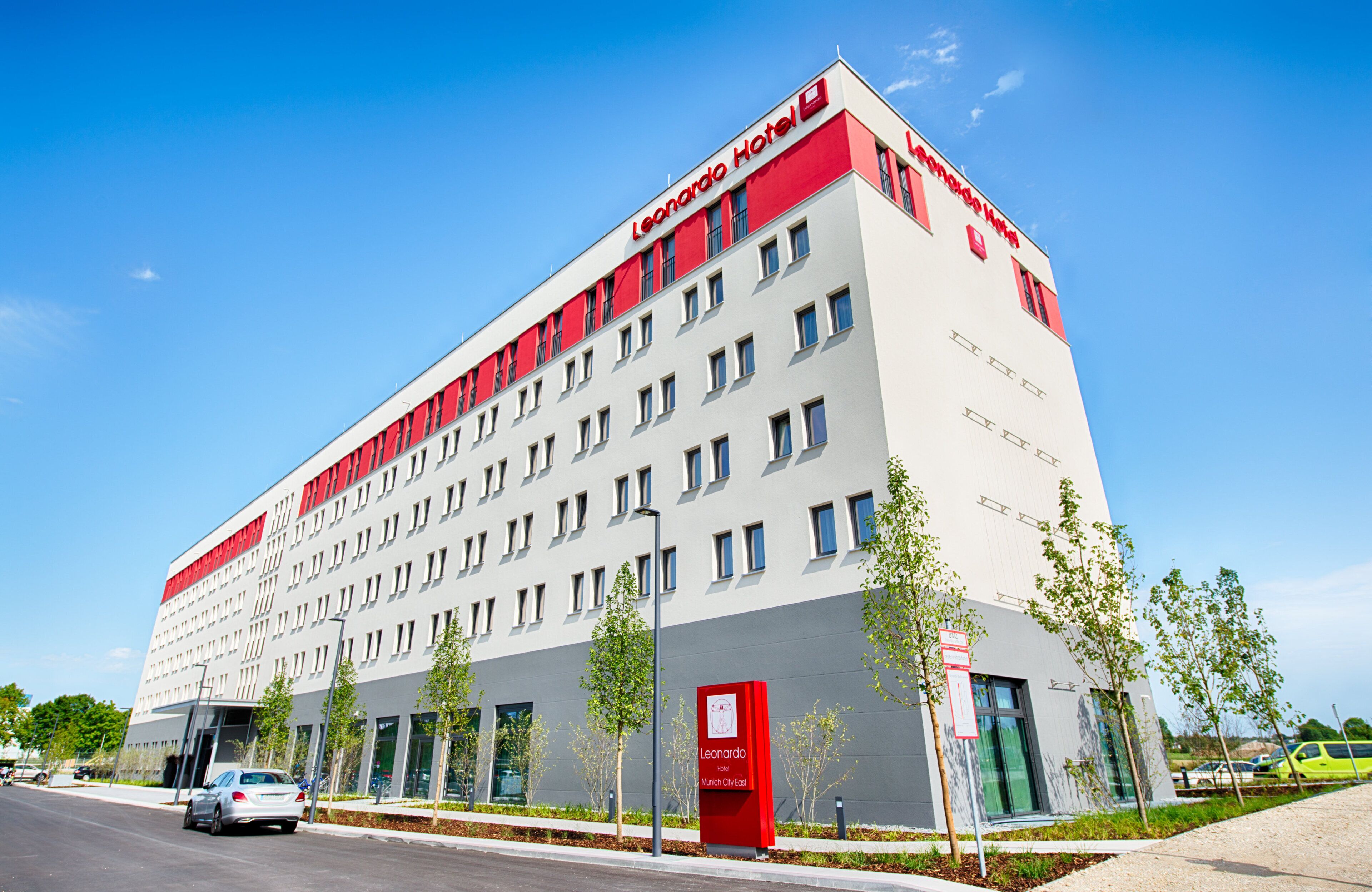 Ein modernes Hotelgebäude mit roter und weißer Fassade, zahlreichen Fenstern und einem Schild, das es als Leonardo Hotel in München-Nord identifiziert.