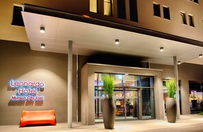 L’extérieur de l’hôtel Leonardo présente un design moderne, avec une entrée imposante, un espace salon et des plantes en pot.