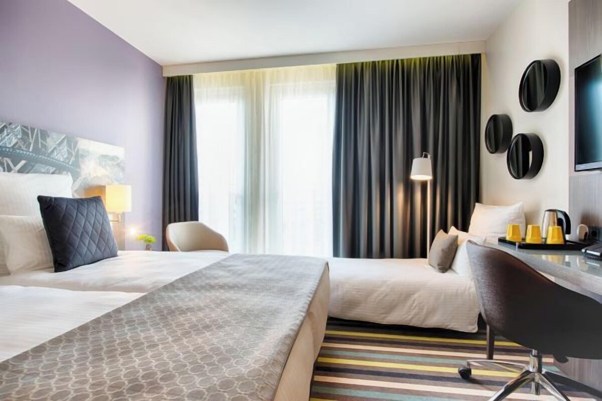 Habitación de hotel con dos camas, un escritorio, una silla, un televisor y una ventana con cortinas.