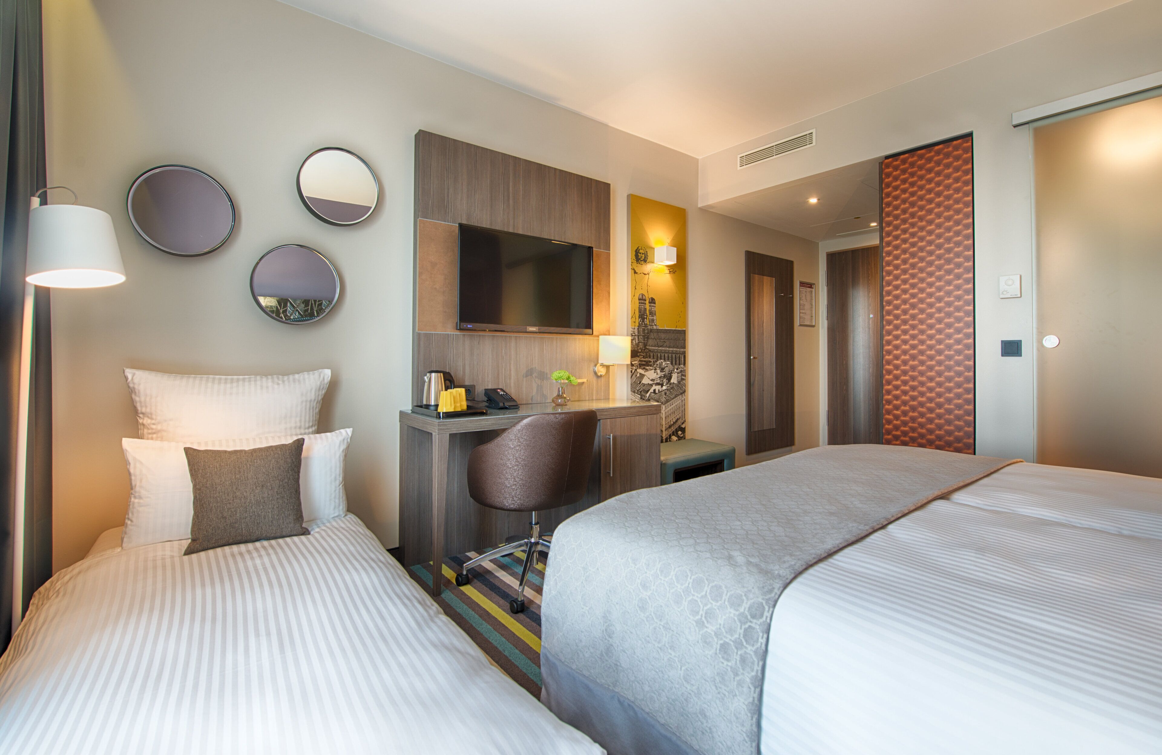 Ein Hotelzimmer mit zwei Betten, einem Schreibtisch, einem Stuhl, einem Spiegel und einem Fernseher.