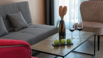 Ein modernes Wohnzimmer mit einem grauen Sofa, einem roten Sessel, einem Couchtisch mit grünen Äpfeln und Weingläsern sowie einer Vase mit dekorativen Zapfen.
