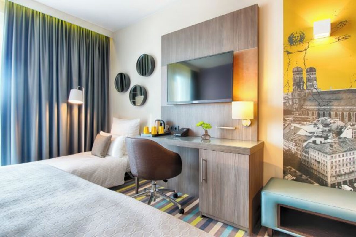 Habitación de hotel con cama, escritorio, silla, televisor y un cuadro en la pared.