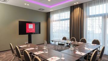 A conference room with a large table, chairs, a flat-screen TV, and a large window with curtains.