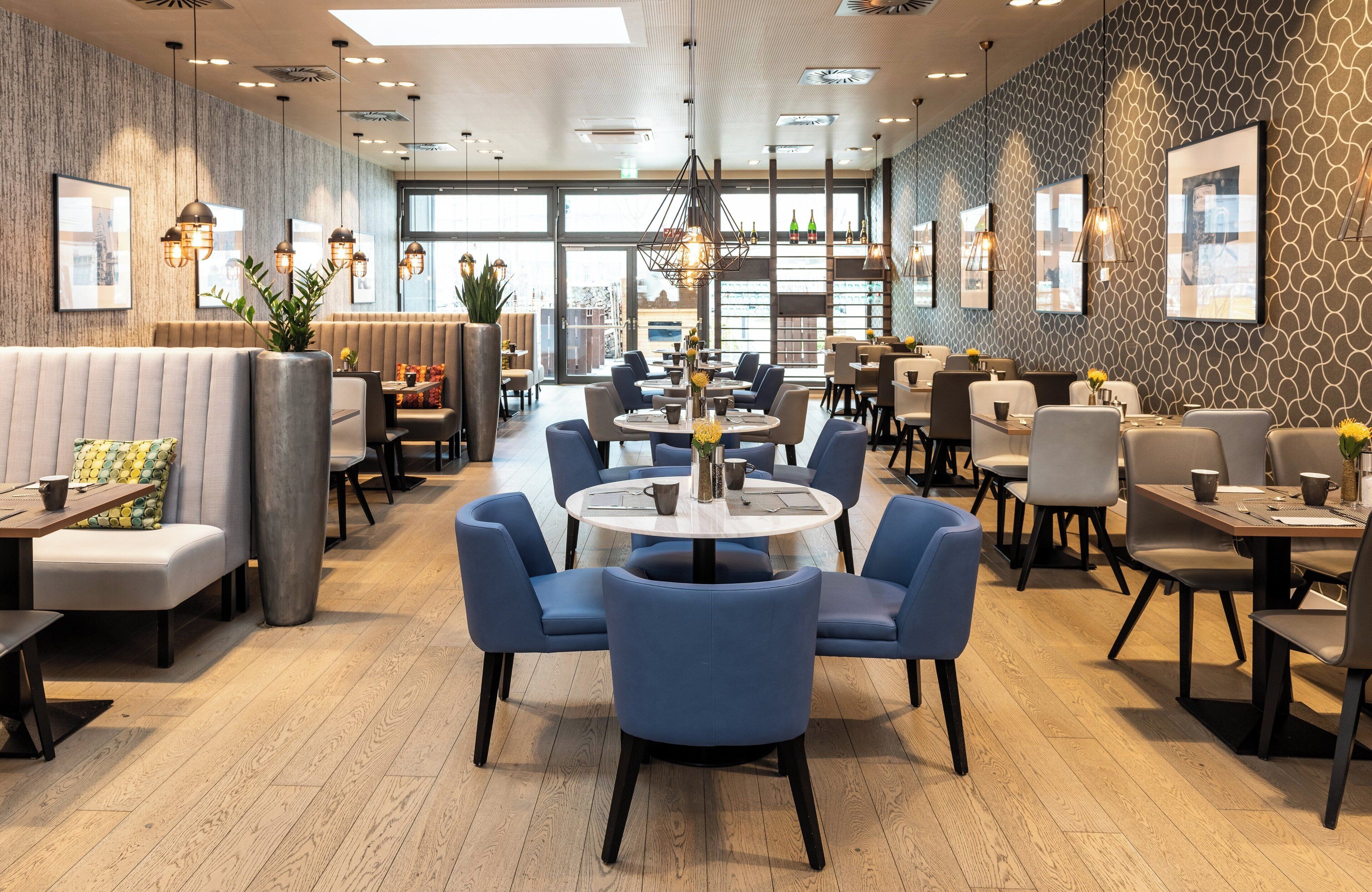 En modern restaurang med runda bord och blå stolar, en bardisk och stora fönster med fin utsikt.