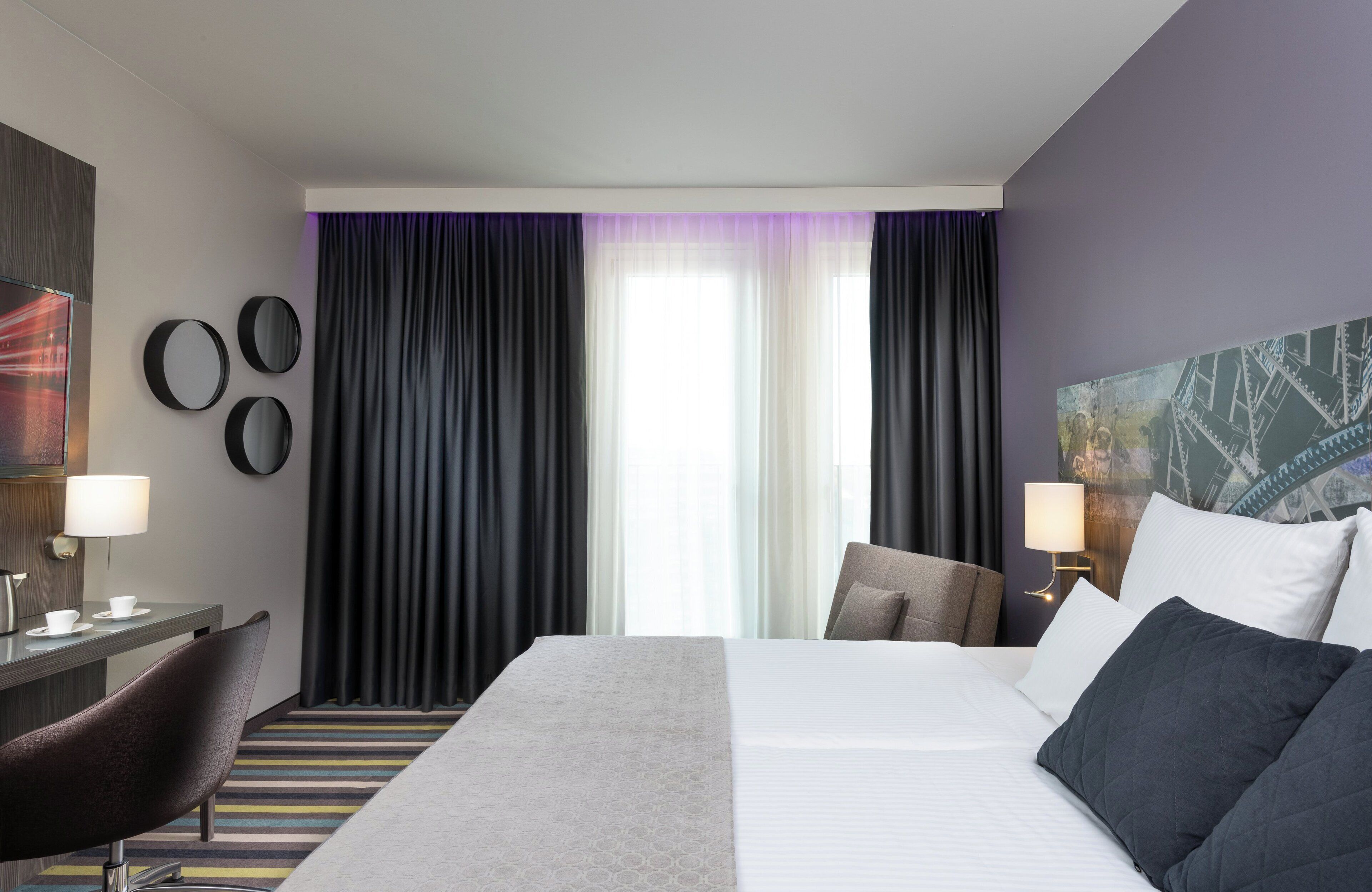 Een hotelkamer met een groot bed, een bureau met stoel, een lamp en een schilderij aan de muur.