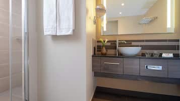 Un baño moderno con cabina de ducha de vidrio, un espejo grande y un tocador oscuro con lavabo blanco.