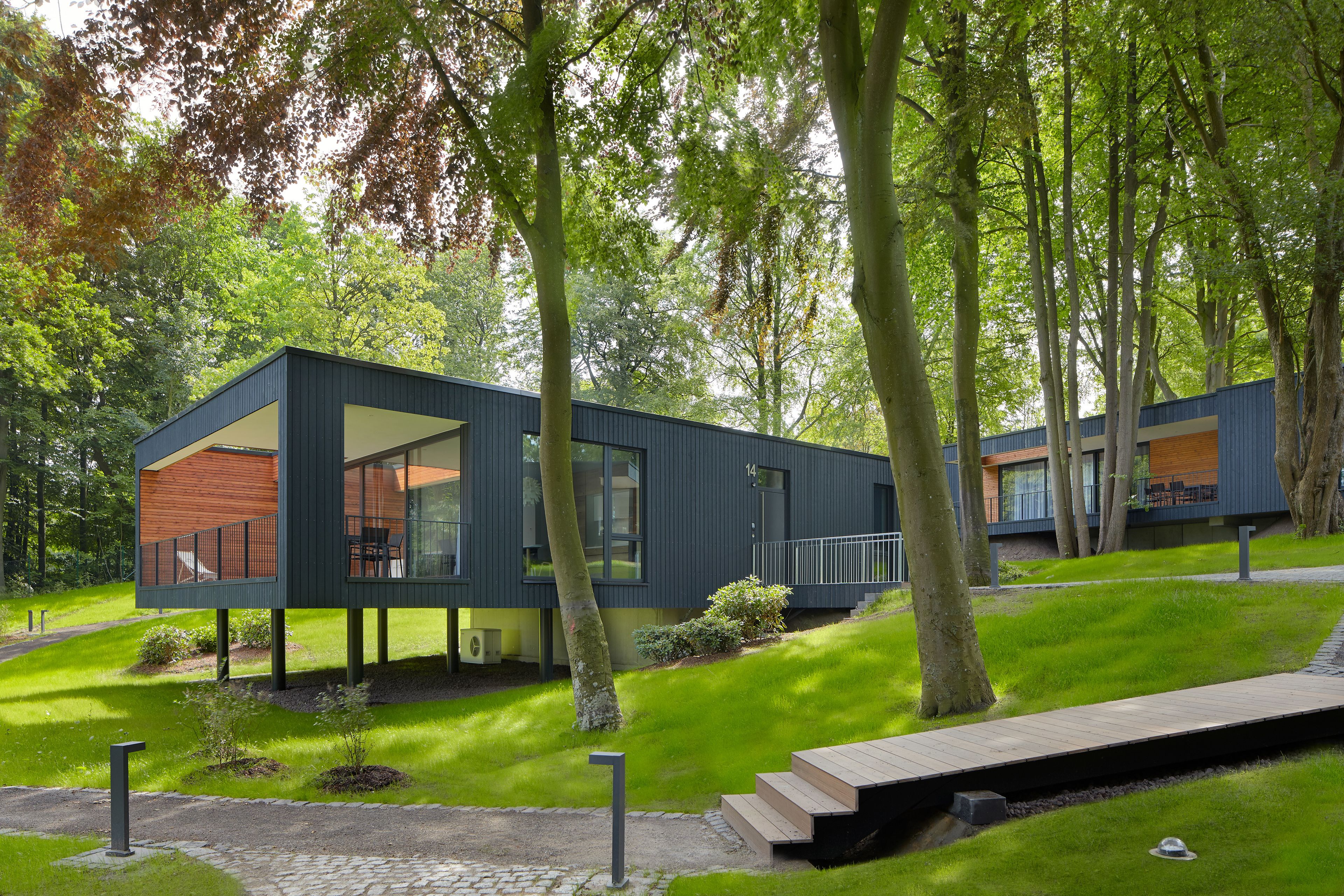 Una casa moderna amb un gran finestral de vidre, envoltada d'arbres i un jardí ben cuidat.