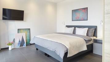 Een moderne slaapkamer met een bed, nachtkastjes, een flatscreen-tv en kunstwerken aan de wanden.