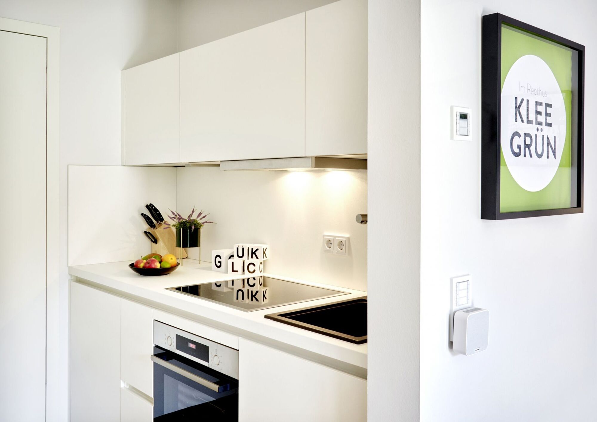 Una cocina moderna con armarios blancos, horno empotrado, fregadero y un cuadro enmarcado en la pared.
