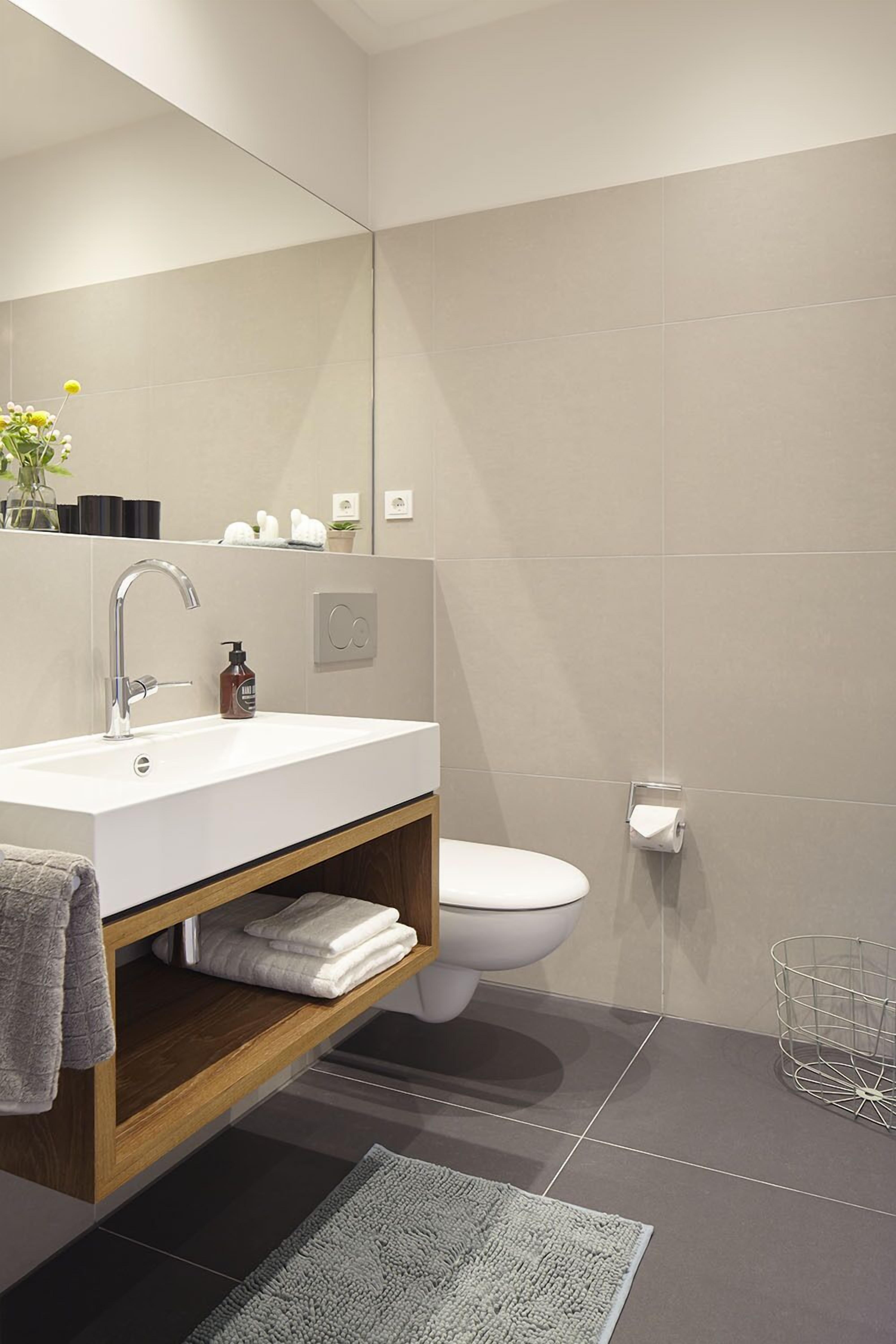 Ein modernes Badezimmer mit Waschbecken, Holzkonsolenunterschrank, Toilette und großem Spiegel.