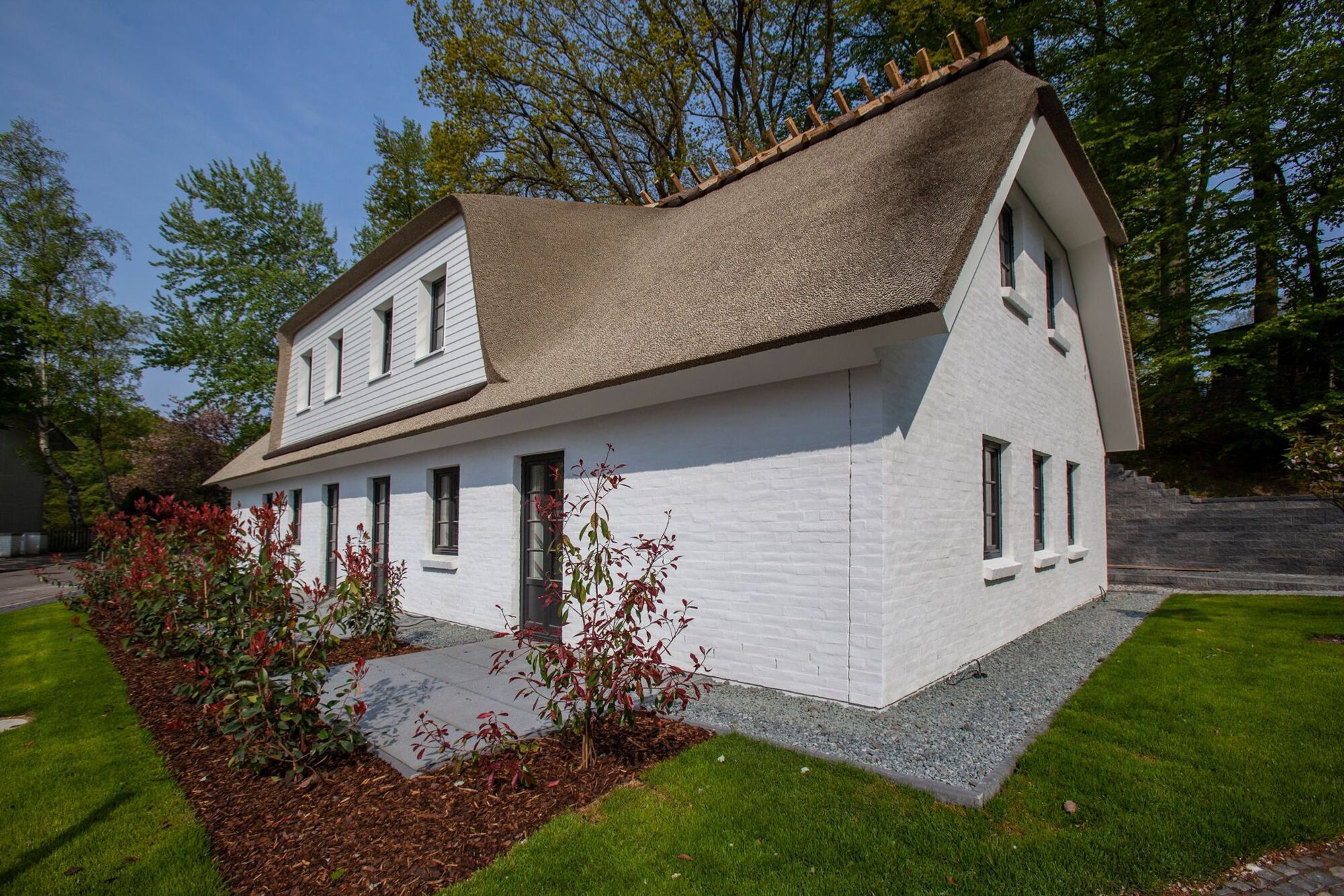 Une maison blanche avec un toit de chaume, un porche à l’avant et un petit jardin.