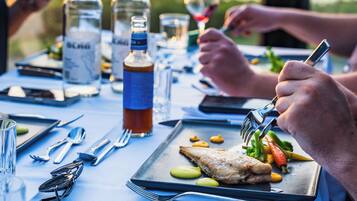 Una mesa de comedor dispuesta con platos, cubiertos y botellas, con vista al agua de fondo.