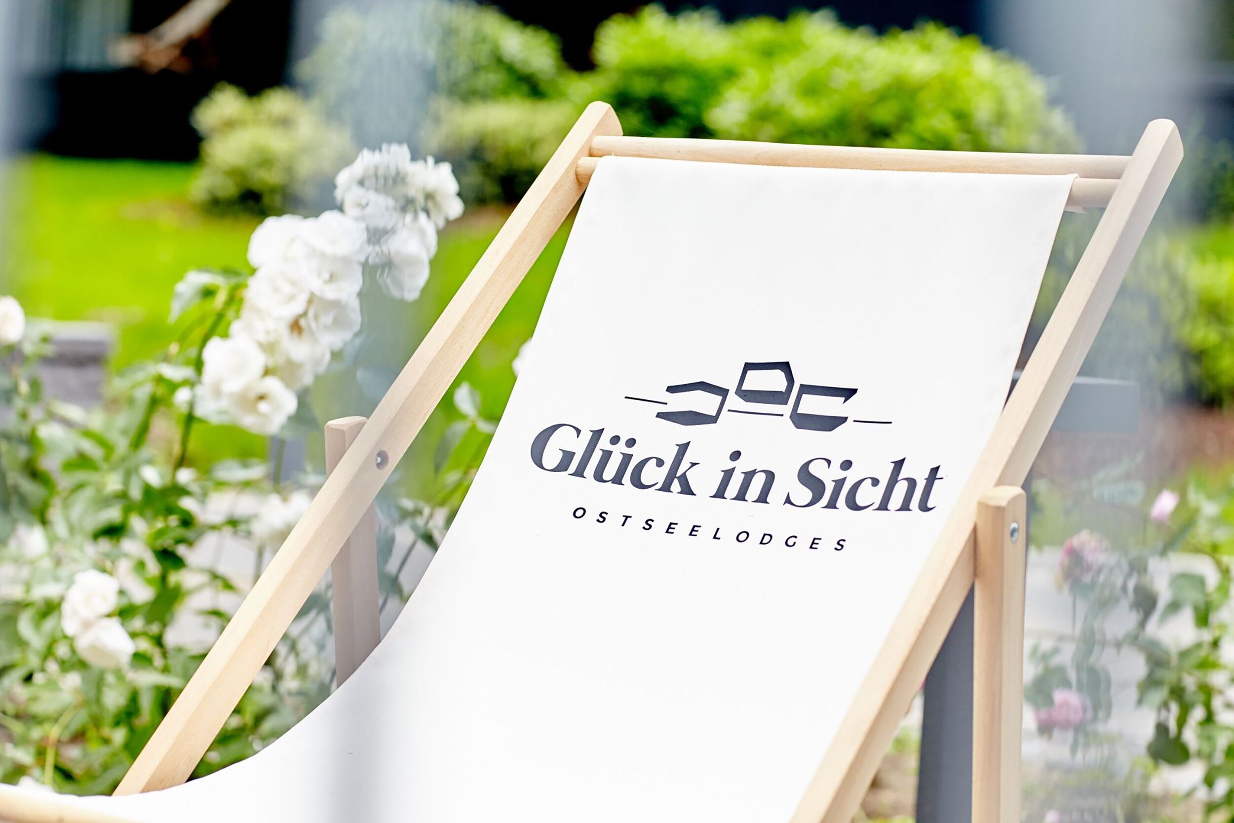 Un chevalet blanc orné d’un logo et de l’inscription « Glück in Sicht OSTSEELODGES », le tout installé dans un jardin.