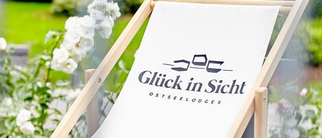 Un chevalet blanc orné d’un logo et de l’inscription « Glück in Sicht OSTSEELODGES », le tout installé dans un jardin.