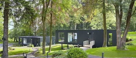 Ein modernes Gebäude mit großen Fenstern und einer flachen Dachkonstruktion, umgeben von üppiger Vegetation und Bäumen.