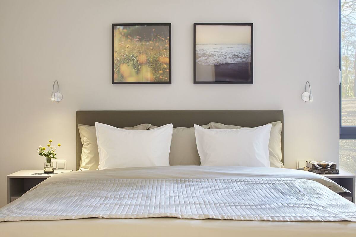 Ein Schlafzimmer mit einem großen Bett, zwei Bildern an der Wand, Nachttischlampen und einem Nachttisch mit einer Blumenvase.
