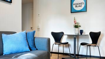 A modern living room with a grey sofa, two black chairs, a small table with a vase and a mug, and a framed picture on the wall.