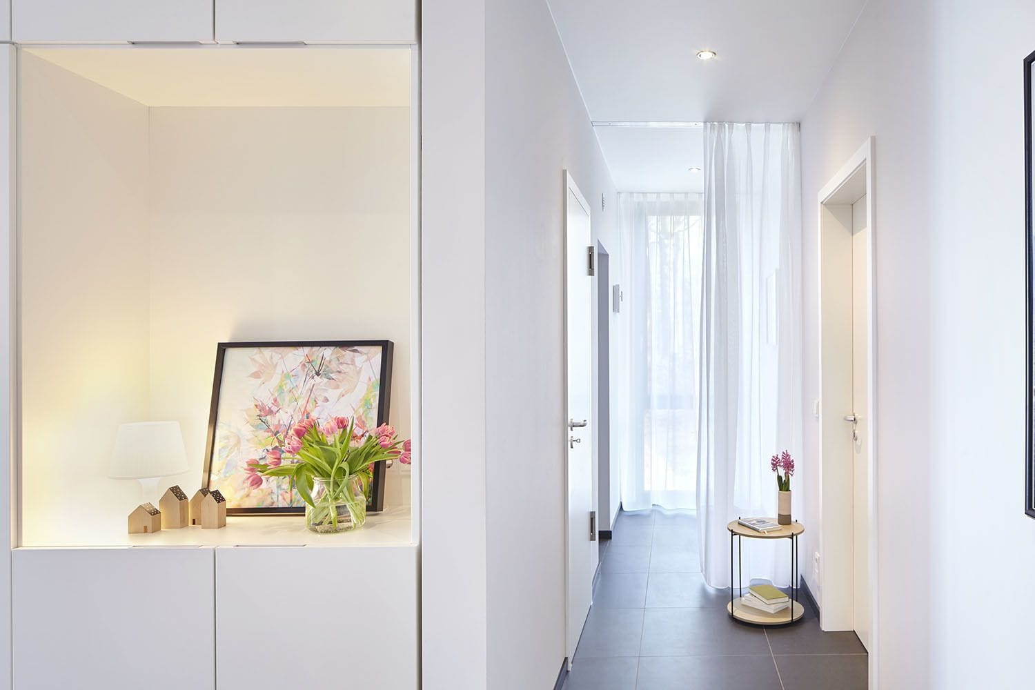 A modern hallway with a framed picture, a vase with flowers, and a small table with books.