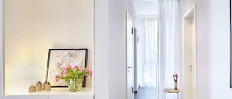 Un pasillo moderno con un cuadro enmarcado, un florero con flores y una pequeña mesa con libros.