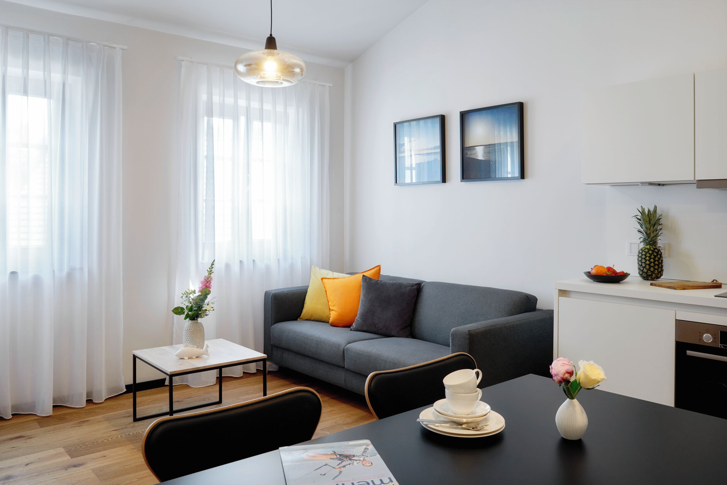 A modern living room with a sofa, dining table, and kitchen area.