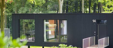 A modern, black cabin with a large window, a small deck, and a staircase leading to the entrance.