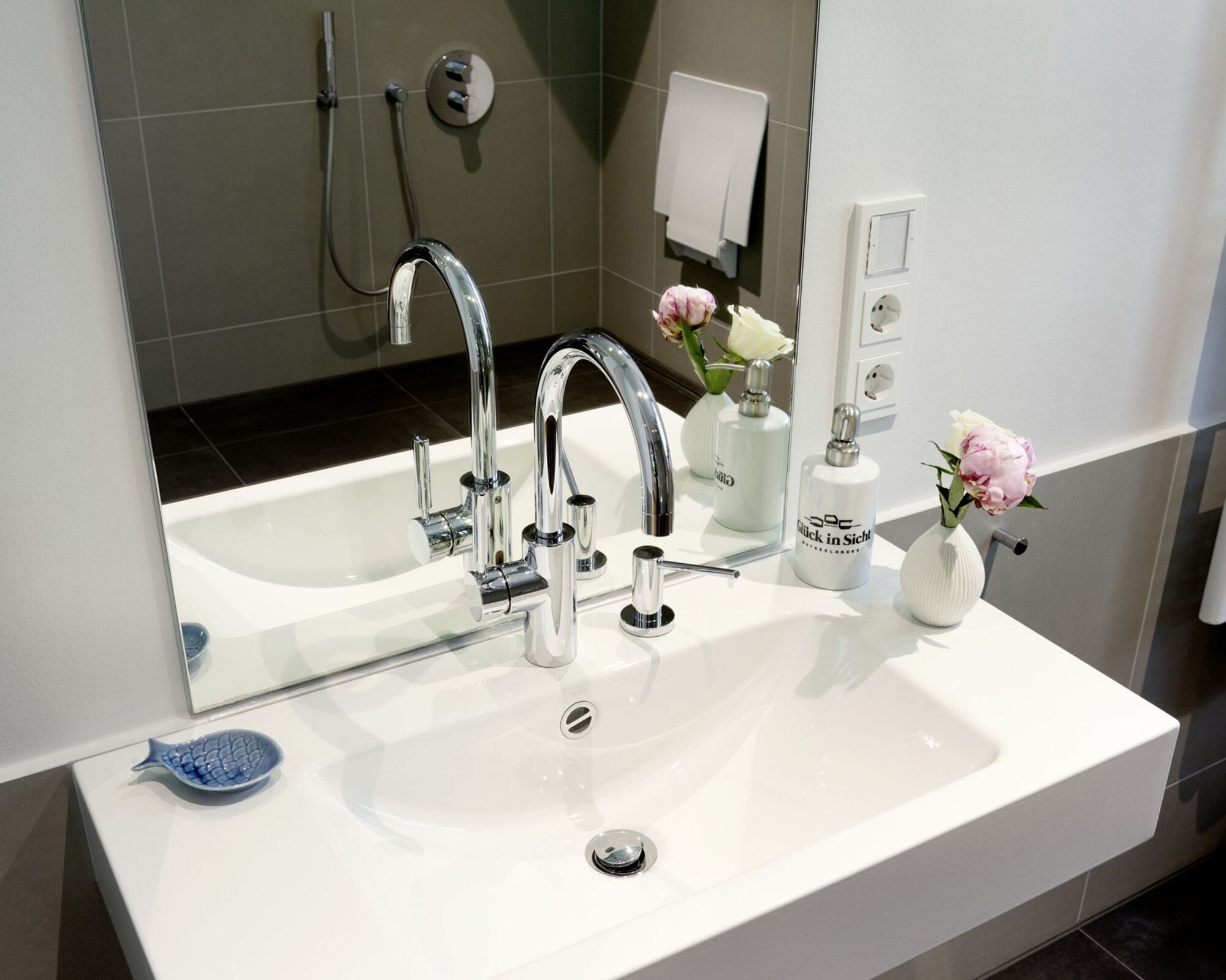 A modern bathroom with a large mirror, chrome faucet, and a white sink.