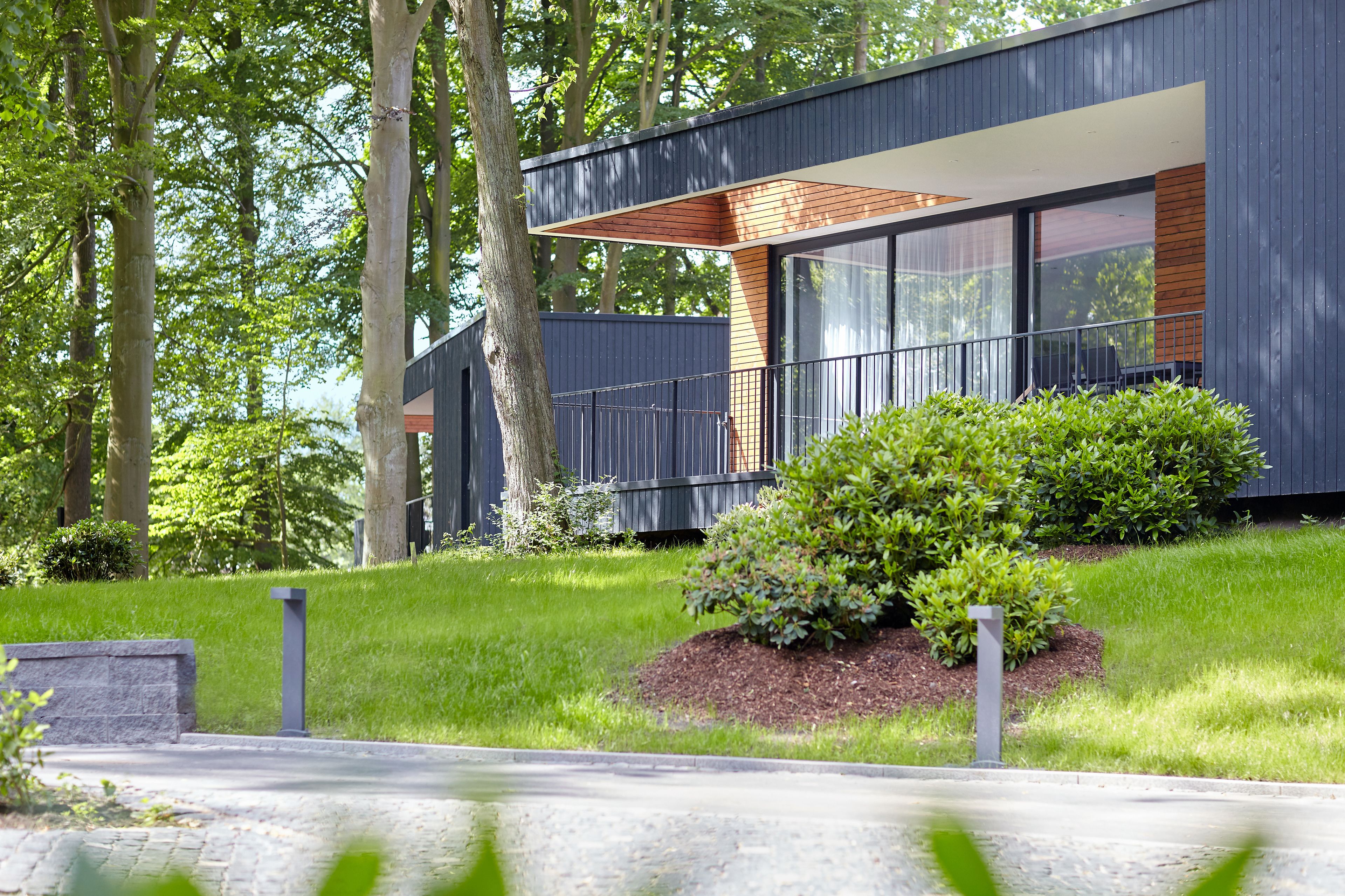 A modern house with large windows, a wooden deck, and a well-maintained lawn.