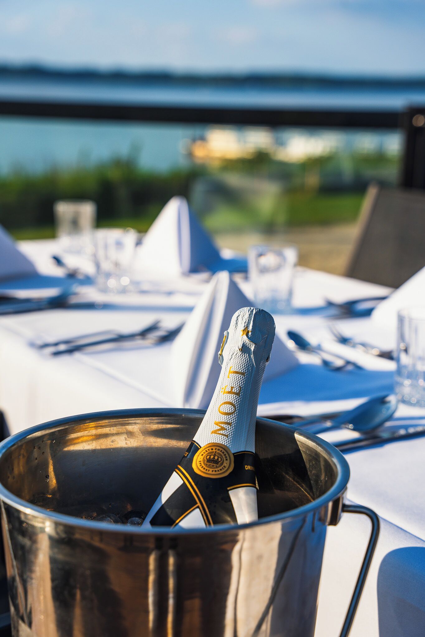 Une bouteille de champagne dans un seau en métal, posée sur une table avec vue sur la mer.