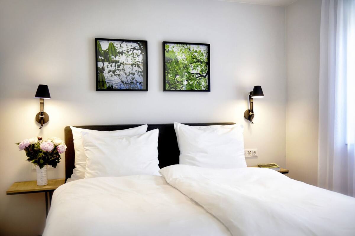 Ein Hotelzimmer mit einem Bett, zwei Wandlampen, einer Blumenvase und zwei gerahmten Bildern an der Wand.