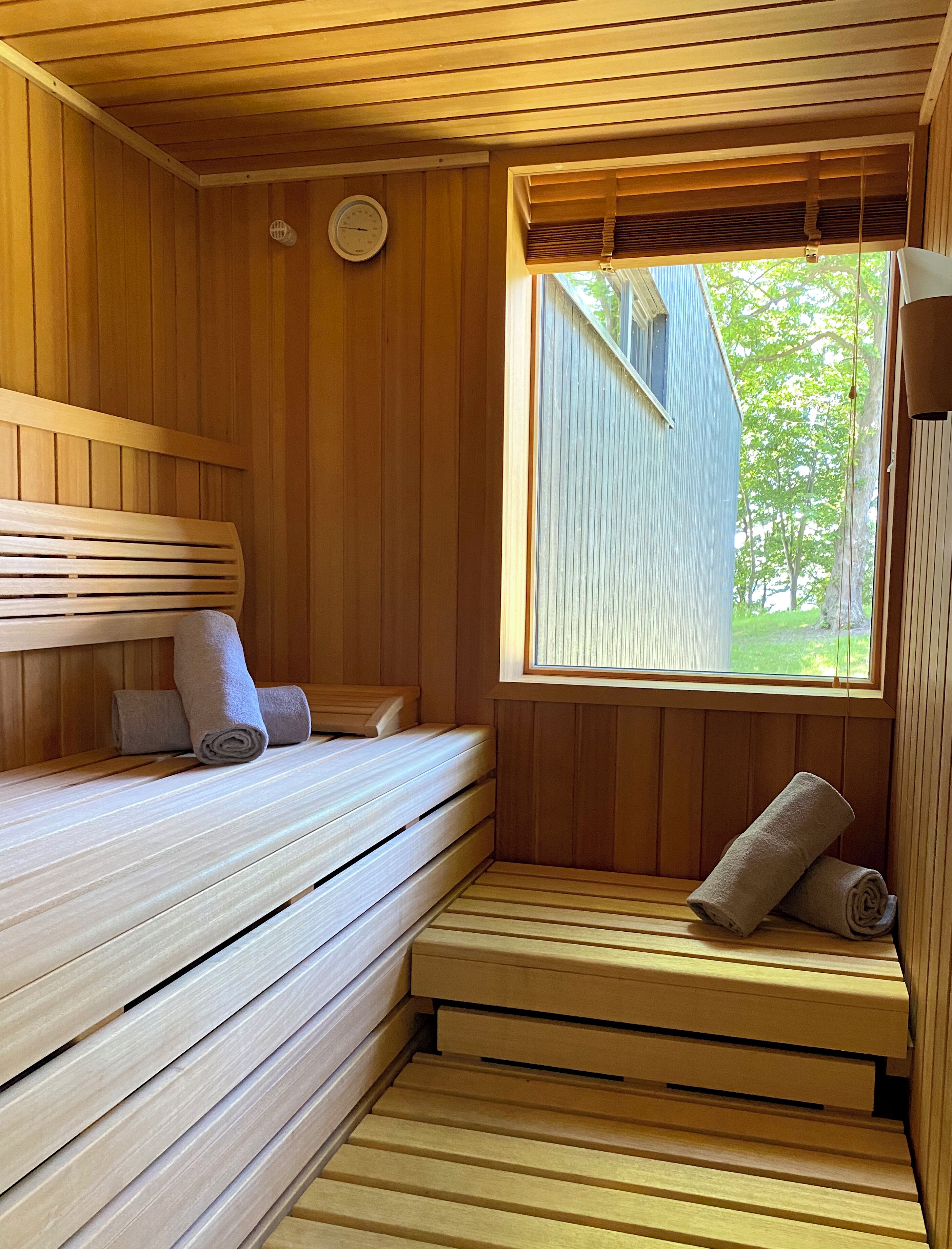 Una sala de sauna con bancos de madera, una ventana con persianas y un reloj de pared.