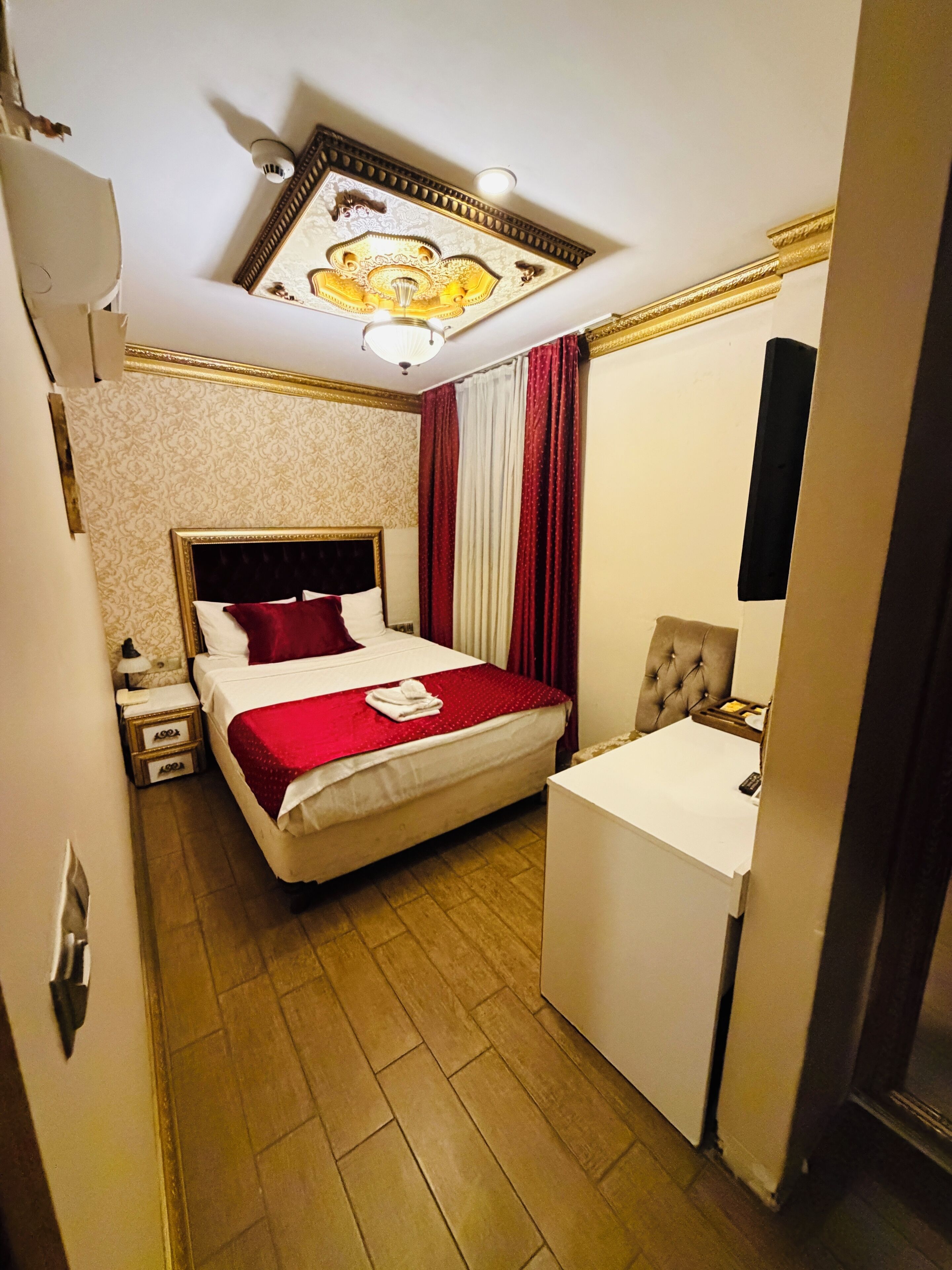 A hotel room with a bed, bedside table, and a small desk with a mirror.