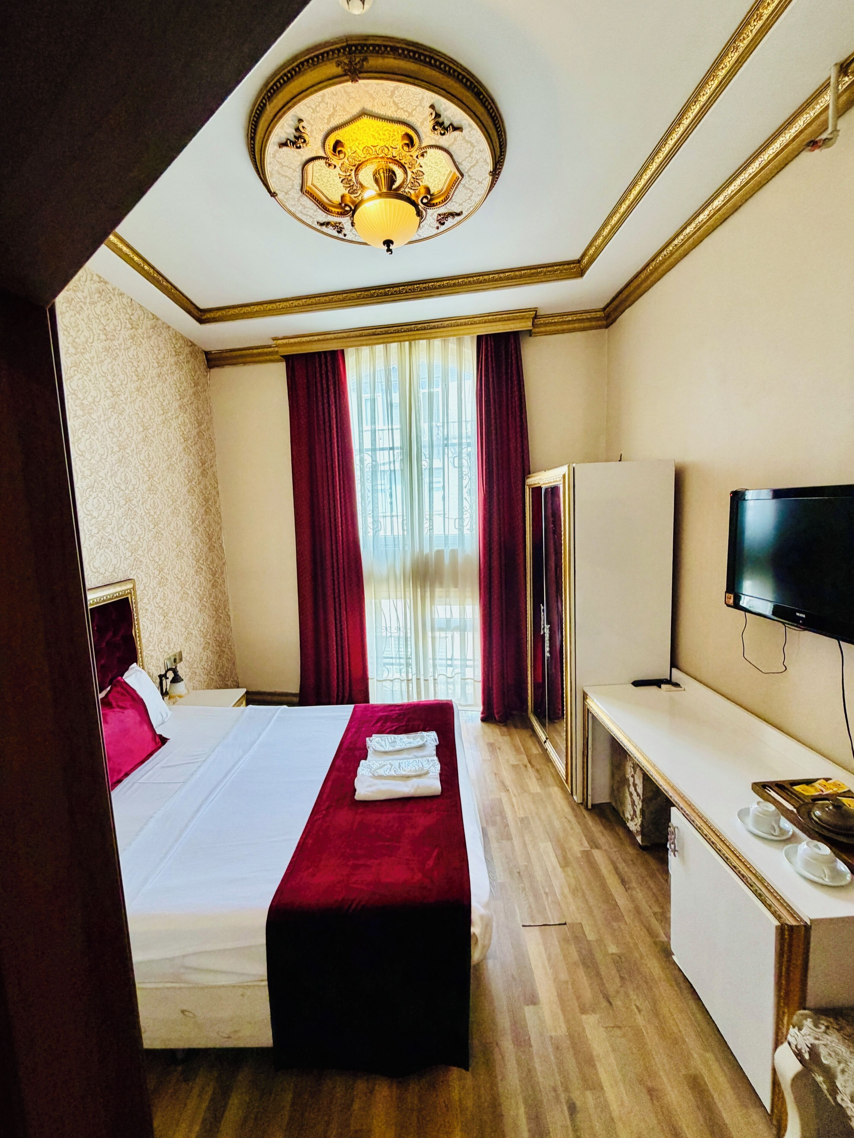 Ein Hotelzimmer mit einem Bett, einem Schreibtisch, einem Fernseher und einem großen Fenster mit Vorhängen.