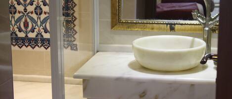 Un bany amb un lavabo de marbre blanc, un mirall amb marc daurat i rajoles amb dibuixos.
