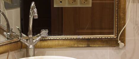 A bathroom with a large white sink, a mirror with a gold frame, and a wooden door in the background.