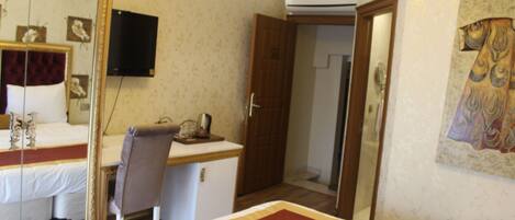 Quarto de hotel com cama, escrivaninha, cadeira, televisão e porta que dá para outro cômodo.
