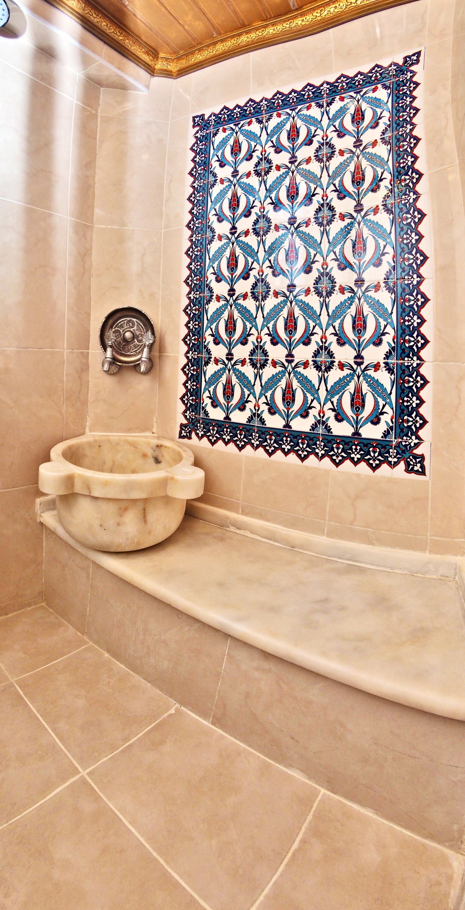 A bathroom with a marble sink, a decorative tile wall, and a small metal object on the wall.