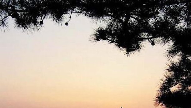 A sunset over a calm body of water with a silhouette of a building and people on the shore. - Qingdao Donghai Hotel (Qingdao)