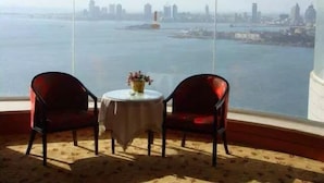 A room with a large window overlooking a city skyline and a body of water. There is a round table with a vase of flowers and two chairs. - Qingdao Donghai Hotel (Qingdao)