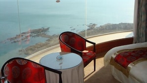 A hotel room with a large window offering a view of the sea and distant mountains. - Qingdao Donghai Hotel (Qingdao)