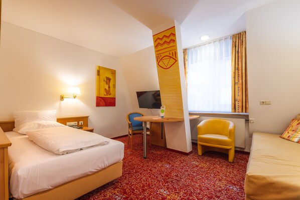Une chambre d’hôtel équipée d’un lit, d’un bureau, d’une chaise, d’une télévision et d’une fenêtre avec des rideaux.
