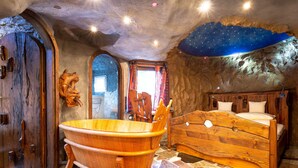 A rustic room with a wooden bathtub, a bed with wooden headboard, and a stone wall. - ALLVITALIS Traumhotel (Karlsruhe)