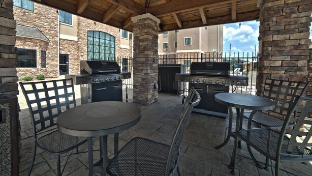 Une terrasse extérieure avec des piliers en pierre, deux barbecues et des chaises en métal.