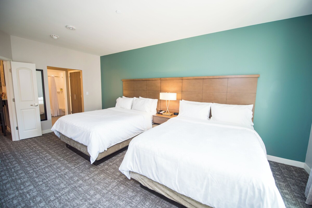 A hotel room with two beds, a bathroom, and a door leading to another room.