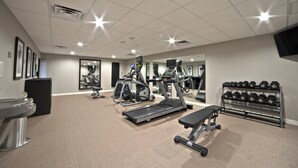 Une salle de sport équipée de tapis de course, de vélos elliptiques, d’un banc et d’un porte-haltères.