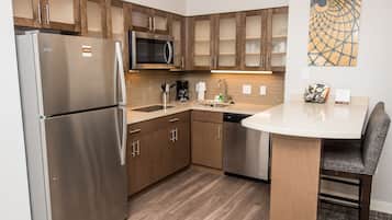 A modern kitchen with stainless steel appliances, wooden cabinets, and a dining area with a round table and chairs.
