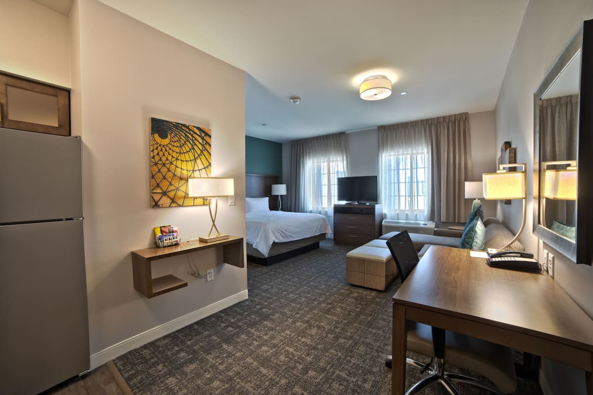 Une chambre d’hôtel équipée d’un lit, d’un bureau, d’une chaise, d’une télévision et d’un réfrigérateur.